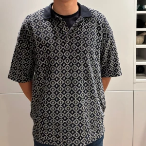 Drole de Monsieur: Mönstrad mörkblå pikéskjorta - Drole de Monsieur ;  mörkblå pikéskjorta med vit rutigt mönster och klassisk krage. Skjortan har korta ärmar och en loose passform som ger en avslappnad vibe. Perfekt för dig som gillar streetstyle och vill sticka ut med ett coolt mönster.