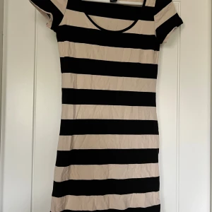 Randig kortklänning med beige och svart - Kortklänning med breda horisontella ränder i beige och svart. Klänningen har rund halsringning och korta ärmar, figurnära passform. Använd fåtal gånger. 