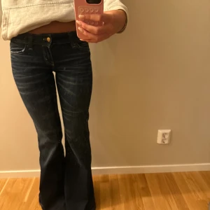 Mörkblå bootcut jeans med låg midja - Snygga mörkblå jeans med bootcut och låg midja. Jeansen har klassiska fickor fram och bak, guldfärgad knapp och diskreta slitningar för en cool look. Perfekta för dig som gillar en retro vibe och vill ha ett par jeans som sticker ut. Storleken är W25/32💗