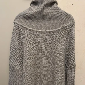 Grå stickad polotröja med slits - Säljer en grå stickad polotröja med hög krage och långärmad design. Tröjan har en snygg slits på sidan och är ribbstickad upptill och vid ärmarna. 