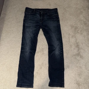 Emporio Armani mörkblå jeans - Snygga mörkblå jeans från Emporio Armani med klassisk femficksdesign och ikonisk logga på bakfickan. Jeansen har raka ben och är tillverkade i mjukt denimtyg som ger en skön passform. Perfekta för dig som gillar stilrena och tidlösa jeans.
