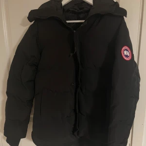 Svart dunjacka från Canada Goose  - Säljer en svart dunjacka från Canada Goose i storlek M. Den är tvärfet och helt ny, alla lappar ingår och jag säljer den då den passar lite för stort på mig annars är den i perfekt skick 