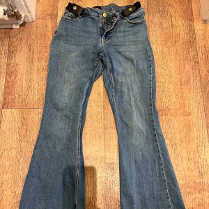 Blå bootcut jeans från Vero Moda - Snygga blå jeans från Vero Moda med bootcut passform och klassisk dragkedja. Jeansen har en normal midja och är tillverkade i mjukt denimtyg med guldfärgade detaljer vid knappen. Perfekta för dig som gillar en retroinspirerad look.