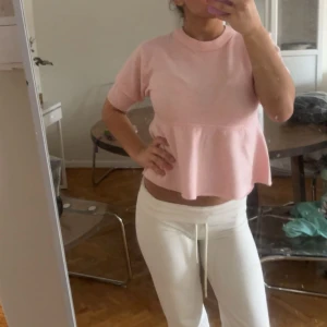 Ljusrosa peplum topp med kort ärm - Supersöt ljusrosa topp med peplumskärning och korta ärmar. Toppen har rund halsringning och är lätt croppad, vilket ger en trendig look. Perfekt att styla med både jeans och kjol för en fräsch vibe.