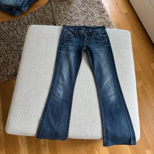Hudson bootcut jeans blå denim - Snygga blå jeans från Hudson med bootcut passform och klassisk femficksdesign. Jeansen har slitna detaljer, markerade sömmar och coola bakfickor med knappar. Längd 76 cm