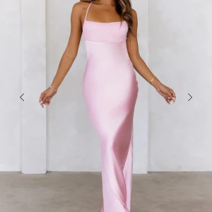 Ljusrosa långklänning med snörning - Supersnygg ljusrosa långklänning i satin med smala axelband och öppen rygg med korsad snörning. Klänningen har en figurnära passform och ett stilrent. Den är helt oanvänd och säljes pga att jag köpte 2 storlekar. Nytt pris är 1350kr men säljer för 700kr+ frakt. Köparen står för frakten.