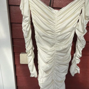 Vit omlottklänning från H&M  - Supersnygg vit kortklänning från H&M med omlottdesign och rynkade detaljer längs hela klänningen. Långa ärmar och glansigt material som ger en lyxig känsla. Perfekt för dig som vill sticka ut med en trendig look. Oanvänd !