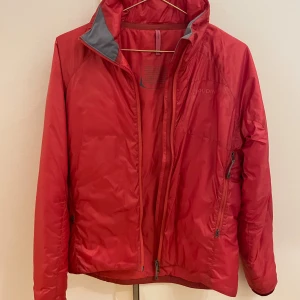 Röd pufferjacka från Houdini - Riktigt snygg röd pufferjacka från Houdini med hög krage och grå detaljer på insidan. Jackan har dragkedja framtill och två sidofickor med dragkedja. Perfekt för kyliga dagar och har en clean, sportig look. Storlek S. Bra skick. 