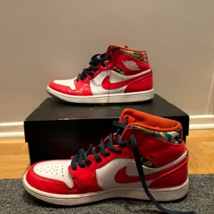 Nike Air Jordan 1 barcelona röd/vit - Nike Air Jordan 1 barcelona sneakers i rött och vitt med svarta skosnören och coolt mönstrat foder i flera färger. Klassisk hög modell med perforerad tå och tydlig Air Jordan-logga på sidan. Ovandel i skinn och syntet, insida med färgglada detaljer.