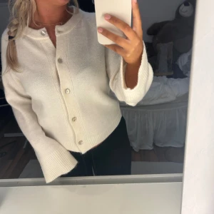 Vit kofta från Gina Tricot - Supermjuk och fluffig vit kofta från Gina Tricot med rund halsringning och snygga knappar framtill. Koftan har långa ärmar med breda ribbade muddar och är perfekt för lager-på-lager. Enkel och stilren design som passar till allt.