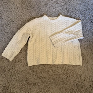 Vit kabelstickad tröja från Zara - Kabelstickad vit tröja från Zara med klassiskt mönster och rund hals. Tröjan har lång ärm och ribbade muddar vid hals, ärmslut och nederkant. Perfekt för lager-på-lager och en clean look.