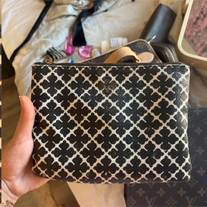 Svart och beige kuvertväska från malene Birger  - Kuvertväska från Morris med ett snyggt grafiskt mönster i svart och beige. Väskan har guldfärgad dragkedja och Morris-logga framtill. Perfekt storlek för att ha med det viktigaste och tillverkad i tåligt skinnmaterial.