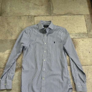 Randig skjorta från Polo Ralph Lauren - Snygg slim fit skjorta från Polo Ralph Lauren i vitt och blått med tunna fina ränder. 