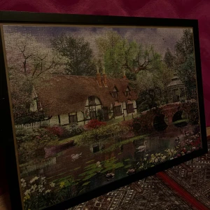 Pyssel i ram - Det här är ett pussel med ett idylliskt motiv av en engelsk stuga vid en damm, omgiven av blommande träd, en stenbro och svanar. Perfekt för dig som gillar natur, avkoppling och vackra landskap. Pusslet är inramat och passar som dekoration i hemmet.