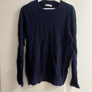 Marinblå stickad tröja från Celio - Snygg marinblå stickad tröja från Celio i storlek L. Tröjan har rund hals och långa ärmar med ribbade muddar. Perfekt för dig som gillar enkel och stilren design. Materialet är mjukt och känns skönt mot huden.