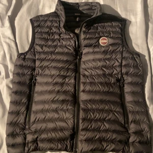 Svart dunväst från Colmar - Snygg svart dunväst från Colmar med quiltad design och dragkedja framtill. Västen har två praktiska fickor med dragkedja och en hög krage. Perfekt för lager-på-lager och har en stilren look med Colmar-logga på bröstet. Pris kan diskuteras!!