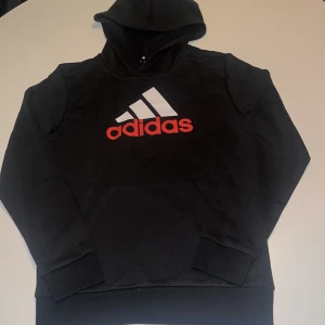 Svart Adidas hoodie med logga - Skön hoodie som är helt ny. Tunn luva och en mag ficka.