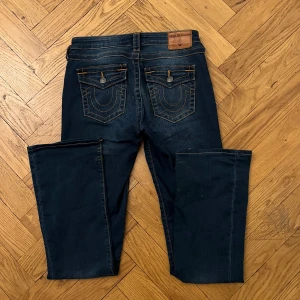 True Religion Becca Bootcut Jeans strl 27 - Mörkblå bootcut jeans från True Religion, modell Becca. Otroligt fina, lågmidjade och bootcut 🔥 Midjemåttet är 37cm tvärsöver och innerbenslängden är 79cm!
