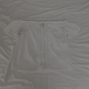  offshoulder blus  - Söt vit offshoulder blus från H&M i storlek XS. Toppen har korta ärmar, spetsdetaljer framtill och en luftig känsla. Perfekt till sommaren och enkel att matcha med jeans eller kjol.