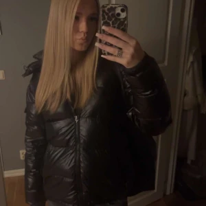 Svart Moncler pufferjacka med huva - Säljer en svart pufferjacka från Moncler med glansig finish och huva. Jackan har dragkedja framtill, fickor med dragkedja och en patch med Moncler-logga på ärmen. Perfekt för kalla dagar och har en riktigt schysst oversized vibe. 