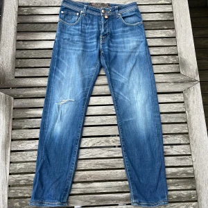  Jacob Cohën jeans med slitningar - Snygga blå jeans från Jacob Cohën med sjukt snygga slitningar. Modellen är slim fit och i size 31. Nyprs ligger runt 3200kr men säljs nu för 749kr. Hör av er vid minsta lilla fundering.