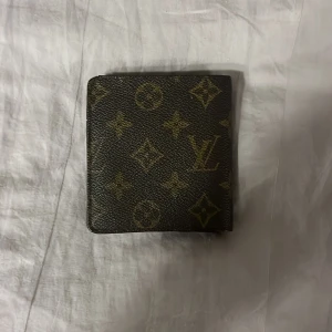 Plånbok  - Snygg plånbok  med klassiskt monogrammönster i brunt och beige. Utsidan är i skinn, insidan har flera fack för kort och ID-fönster i ljust brunt läder. Perfekt för dig som vill ha något lyxigt och stilrent.