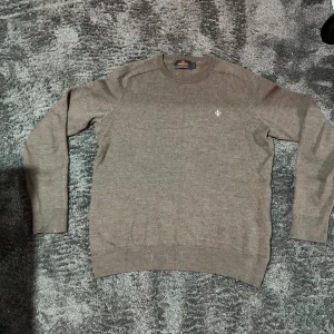 Brun stickad tröja från Morris - Säljer en brun stickad tröja från Morris med rund halsringning och diskret logga broderad på bröstet. Tröjan har ribbade muddar vid ärmslut och nederkant, perfekt för lager på lager under kyliga dagar.