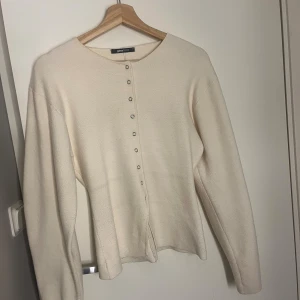 Beige kofta från Gina Tricot - Snygg beige kofta från Gina Tricot med rund hals och långa ärmar. Koftan har en rak passform och knäpps med små silvriga knappar framtill. Mjuk och skön, perfekt att slänga på sig när det är lite kyligt ute.