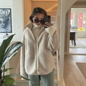 Beige teddyjacka - Säljer en beige teddyjacka med hög krage och hel dragkedja framtill. Jackan har en loose passform och är tillverkad i mjuk fleece som ger en chill och cozy vibe. Perfekt att slänga på sig när det är kallt ute. Långärmad och enkel att styla till olika outfits.