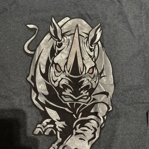 Mörkgrå Ecko Unltd t-shirt med noshörning - Snygg mörkgrå t-shirt från Ecko Unltd med stor, silvrig noshörningsgrafik på bröstet. Klassisk rund hals och korta ärmar. Tillverkad i en mjuk mix av bomull och polyester, perfekt för en streetwear-look.