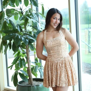 Champagnefärgad paljettklänning - Supersnygg kort klänning i champagnefärg med massor av paljetter. Klänningen har breda axelband, markerad midja och utställd kjol. Perfekt för dig som vill sticka ut med glittrig look och trendig passform. Säljs utan accessoarer.