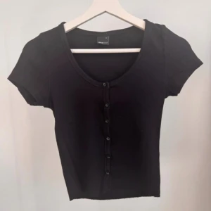 Ribbad topp med knappar från Gina Tricot - Svart ribbad topp med knappar från Gina Tricot. Storlek S. Använt fåtal gånger, är i mycket bra skick.