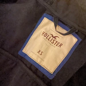 Mörkblå parkajacka Hollister XS - Snygg mörkblå jacka från Hollister i storlek XS. Jackan har både dragkedja och knappar framtill, samt ett broderat Hollister-märke på bröstet. Modellen är långärmad . Perfekt för dig som gillar stilren och klassiskt.💕