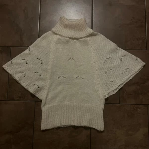 Vit stickad polotröja med vida ärmar i ullmix - Supermysig vit stickad polotröja med bred ribbad krage och korta, vida ärmar. Tröjan har ett diskret hålmönster på ärmarna och är tillverkad i en mjuk blandning av ull, akryl och polyamid. Ingen storleksetikett men den passar som en S.