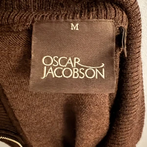 Brun stickad half zip från Oscar Jacobson - Snygg brun stickad tröja från Oscar Jacobson med half zip och kort krage. Perfekt för lager-på-lager och passar till jeans eller chinos. Tröjan har lång ärm och ribbade muddar för en clean look. 100% mjuk ull 