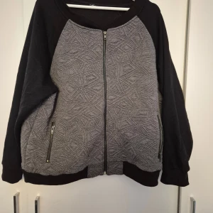 Gråmönstrad kofta från Cubus - Säljer en grå och svart kofta från Cubus med geometriskt mönster framtill. Koftan har hel dragkedja, svarta ärmar och muddar samt två fickor med dragkedja. Materialet är en mix av polyester och bomull med lite stretch för extra komfort. Lappen är borta så osäker på storleken men tror den är i L/XL