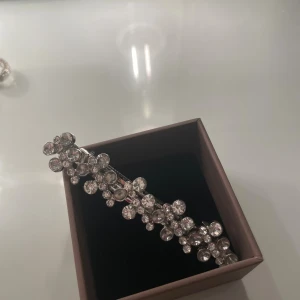 Glittrigt silverfärgat hårspänne - Snyggt hårspänne  i silverfärg med massor av glittrande stenar i olika storlekar. Designen är modern och sticker ut med sitt glittriga uttryck. Perfekt för dig som gillar att glänsa och vill ha något som drar blickarna till sig.