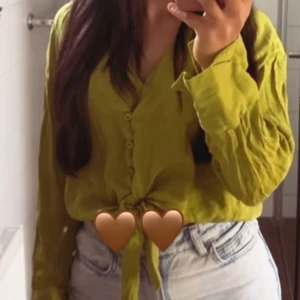 Ljusgul knytblus med knappar - Snygg ljusgul skjorta med knyt framtill och knappar längs bröstet. Långärmad och i ett luftigt material som passar perfekt till jeans. Skjortan har en avslappnad passform och v-ringad hals.