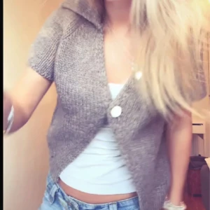 Beige stickad kofta med kort ärm - Säljer en beige stickad kofta med korta ärmar och två stora knappar framtill. Koftan har en bred krage och är perfekt att slänga över ett linne eller t-shirt. Enkel och snygg att styla till jeans eller kjol.