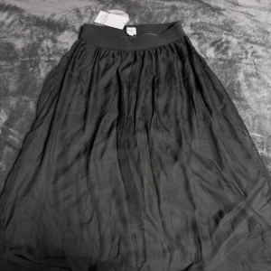 Svart långkjol från Saint Tropez - Svart långkjol från Saint Tropez med bred resår i midjan. Kjolen har ett tunt, skirt yttertyg och ett mjukt innertyg som ger ett snyggt fall. Perfekt för dig som gillar en klassisk och stilren look.