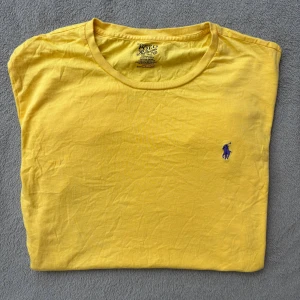  Polo Ralph Lauren T-shirt  - Snygg gul t-shirt från Polo Ralph Lauren med klassisk rund hals och den ikoniska lilla blå polospelaren broderad på bröstet. Tillverkad i mjuk 100% bomull och har en normal passform. Perfekt för dig som gillar stilrena och färgglada plagg.