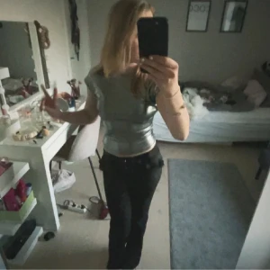 Silvrig croppad topp med öppen rygg - Säljer en silvrig croppad topp med korta ärmar och riktigt snygg öppen rygg. Materialet är glansigt och stretchigt, vilket gör att den sitter tight och framhäver figuren. Perfekt för dig som vill sticka ut med en cool metallic-look. Helt perfekt festtopp