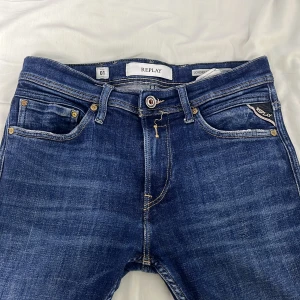 Blå Replay Jondrill jeans - Säljer ett par snygga Replay Jondrill jeans i klassisk blå tvätt. Jeansen har fem fickor, tydliga kontrastsömmar och läderpatch bak i midjan. Modellen är slim och sitter tajt längs benen. Perfekta för dig som gillar en modern och stilren look.