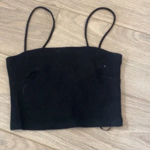 Svart ribbad linnetopp med smala band - Svart croppad linnetopp med smala axelband och ribbad struktur. Enkel och stilren design som funkar till många olika looks. Perfekt för dig som gillar minimalistiska plagg med en modern touch.