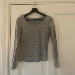 Grå långärmad topp från 157 - En enkel och stilren grå långärmad topp från 157. Modellen har rund halsringning och är tillverkad i mjuk bomull som känns skön mot huden. Perfekt att matcha med jeans eller kjol för en clean look.