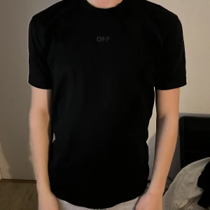 Svart Off-White t-shirt med tryck - Svart t-shirt från Off-White med diskret 'OFF' tryck framtill och stort svart grafiskt tryck på ryggen. Klassisk passform och rund halsringning. Tillverkad i mjuk bomull, perfekt för en stilren streetwear-look. Storleken är S men den är stor i storleken.