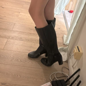 Svarta stövlar med klack från Gabor - Snygga svarta stövlar från Gabor i skinnimitation med rund tå och markerad blockklack. Stövlarna har dragkedja på insidan och en diskret metallogo på sidan. Perfekta för dig som vill ha en klassisk och stilren look. Inte äkta skinn! 💕