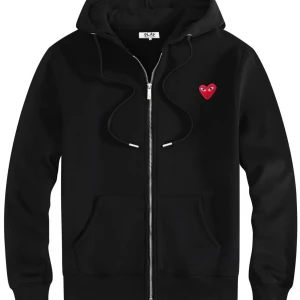 Svart hoodie från Comme des Garçons Play - Svart hoodie med dragkedja från Comme des Garçons Play. Tröjan har huva med snörning, fickor framtill och det ikoniska röda hjärtat broderat på bröstet. Perfekt för en chill och stilren look.