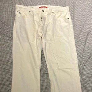 Vita raka jeans från Lacoste - Säljer ett par klassiska vita Lacoste jeans med rak passform och fem fickor. Byxorna har knappgylf och lacoste etikett bak i midjan. Perfekt för dig som gillar tidlös stil och vill sticka ut med ljusa jeans.