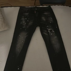 Svarta jeans från Dsquared2 med splatter - Säljer ett par svarta jeans från Dsquared2 i storlek 34. De har coola vita splatterdetaljer och slitningar på framsidan för en edgy look. Klassisk femficksmodell med Dsquared2-lapp bak i midjan. Perfekta för dig som gillar streetstyle. OBS den e större än de andra fast de står storlek 34.
